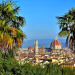Blick von einer Anhebe aus auf die Kathedrale von Florenz. Links und rechts je eine Palme - dahinter das Stadtbild mit dem Dom in der Mitte.