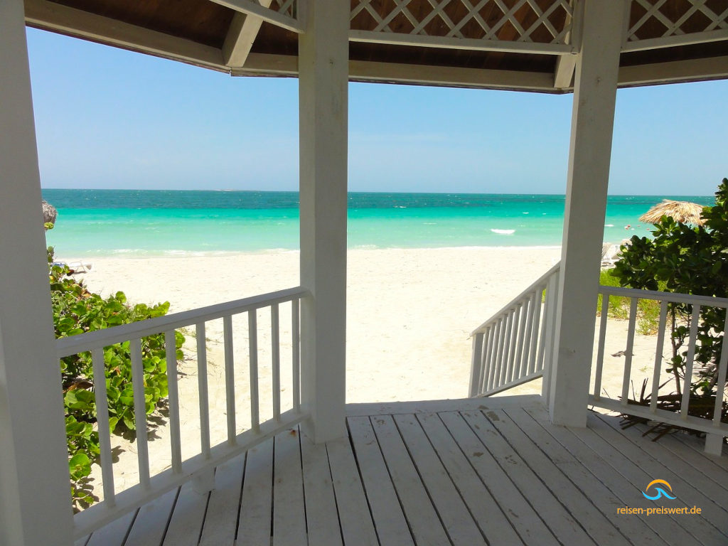 Eine Überdachte Terrasse am Strand von Varadero (Kuba) spendet Schatten. Eine Treppe führt zum weißen Sandstrand. Etwas weiter hinten ist das blaue Meer gut sichtbar