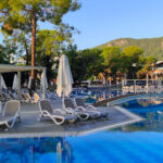 Der Pool im Hotel Rixos Sungate in Kemer. Auf der anderen Seite stehen Liegen und Sonnenschirme. Eine Brücke geht über den Pool und im Hintergrund ist ein Berg mit Bäumen zu erkennen