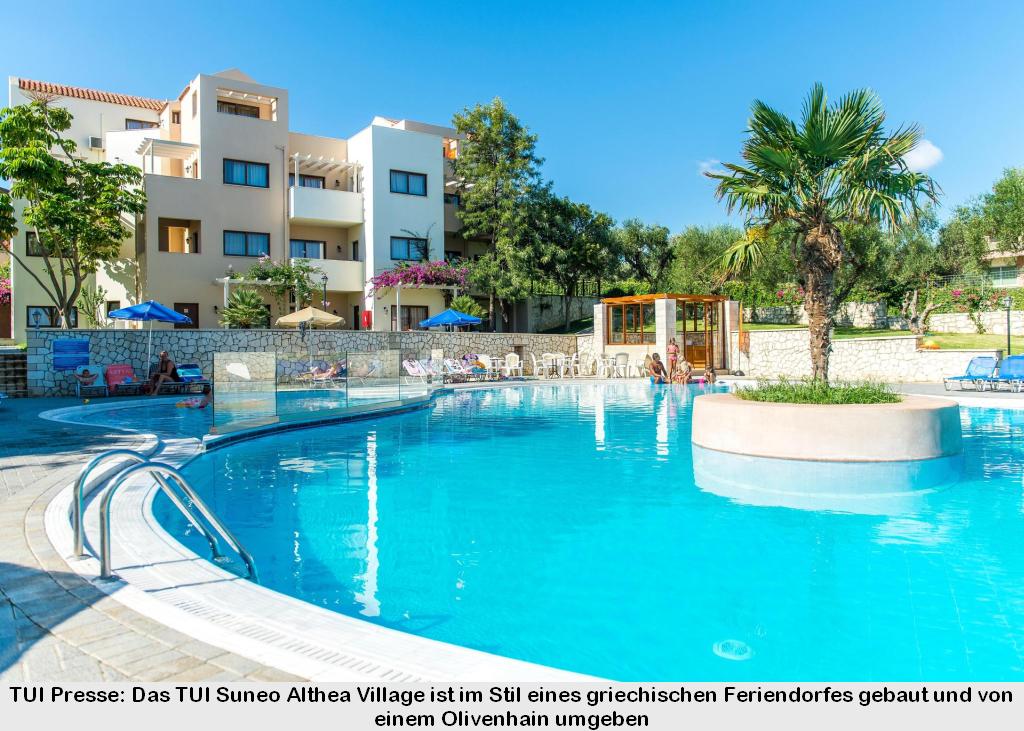 Das TUI Suneo Althea Village ist im Stil eines griechischen Feriendorfes gebaut und von einem Olivenhain umgeben. Im Vordergrund der Pool mit Palmen. Im Hintergrund die gemütlichen Gebäude
