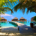 Malediven - Villen am Strand auf Veligandu. Ein Steg führt vom Strand über das blaue Wasser zu den Villen. Diese stehen auf Stelzen im Meer
