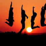 Vier Personen springen in die Luft. Im Hintergrund ist der Sonnenuntergang