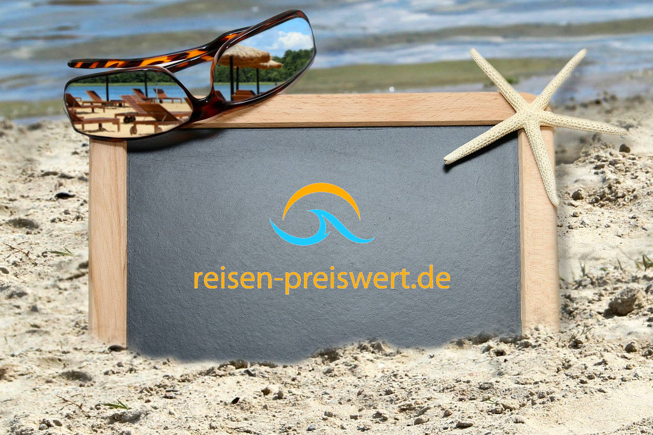 Eine Schiefertafel steckt im weißen Sandstrand. Oben rechts ist eine Sonnenbrille drauf und rechts ein heller Seestern. Der Schriftzug lautet "reisen-preiswert.de"