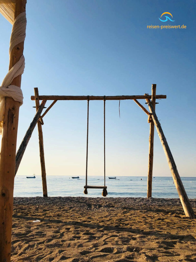 Eine Schaukel am feinen Sandstrand mit Blick auf das Meer in der Abenddämmerung